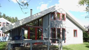 A small, single-story house with a sloped roof, a porch with a table and chairs, and a chimney. - skandinavisches Ferienhaus in Mirow (Granzow)