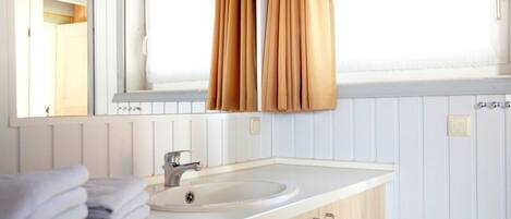 A bathroom with a white sink, a mirror, and a window with curtains.