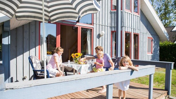 A wooden deck with a table and chairs, a railing, and a house with red-framed windows. - skandinavisches Ferienhaus in Mirow (Granzow)
