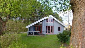 Ein zweistöckiges Haus mit einem geneigten Dach, einer Veranda mit einer Bank und einem kleinen Garten.