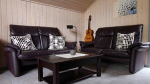 Ein Wohnzimmer mit zwei dunklen Ledersofas, einem Holztisch und einer Gitarre an der Wand.