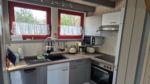 Cocina compacta con lavavajillas, estufa, microondas y ventana con cortina.