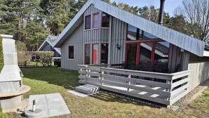Una casa moderna con techo inclinado, una puerta roja y una terraza con barandillas.