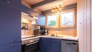 A compact kitchen with blue cabinets, a built-in oven, a dishwasher, and a window above the sink. - Ferienhaus im skandinavischen Stil (Granzow)