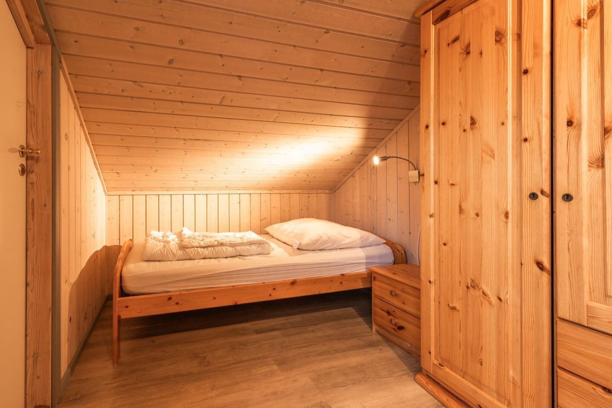 Um quarto pequeno e aconchegante com uma beliche de madeira, um guarda-roupa de madeira e teto inclinado.