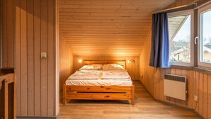 A wooden cabin bedroom with a bed, a window with curtains, and a radiator. - Ferienhaus im skandinavischen Stil (Granzow)