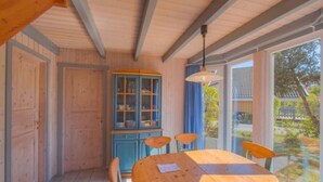 Un'area pranzo in legno con un tavolo rotondo e sedie, un armadietto con ante in vetro e vista sull'esterno attraverso ampie finestre.