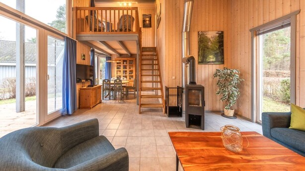 Un vaste espace de vie avec un intérieur en bois, une cheminée et un balcon donnant sur la cour.