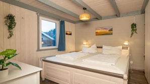 A bedroom with a double bed, a bedside table, a hanging plant, and a window with a view of a house. - skandinavisches Ferienhaus in Mirow (Granzow)