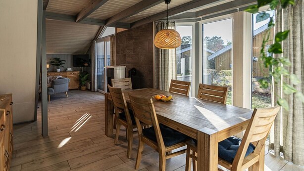 A dining area with a wooden table and chairs, a hanging light fixture, and a view of the outdoors through large windows. - skandinavisches Ferienhaus in Mirow (Granzow)
