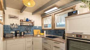 A kitchen with white cabinets, a blue backsplash, a built-in oven, and a hanging light fixture. - skandinavisches Ferienhaus in Mirow (Granzow)