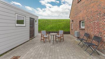 Une terrasse avec une table et des chaises, un mur en briques et, au fond, un champ d’herbe.