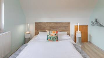 A bedroom with a wooden headboard, white bedding, a colorful pillow, bedside tables with lamps, and a radiator.