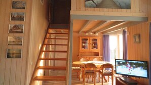 A wooden interior with a staircase, dining area, and a TV.