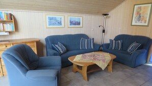 Un saló amb dos sofàs blaus, una taula de centre de fusta, una prestatgeria i quadres amb marc a la paret.