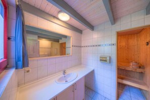 Une salle de bain avec un lavabo blanc, un miroir et un sauna en bois.