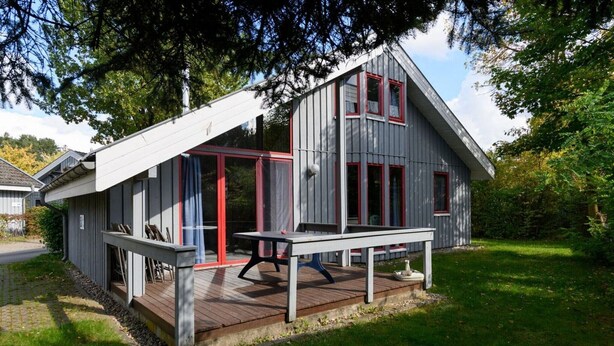 A modern cabin with a deck, large windows, and a red door.