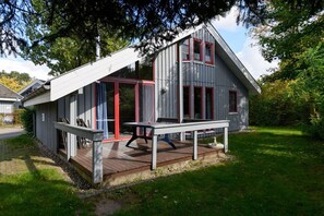 A modern cabin with a deck, large windows, and a red door.