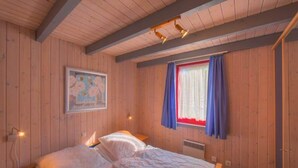 A wooden-paneled room with a bed, a nightstand, a wall-mounted lamp, and a window with curtains.