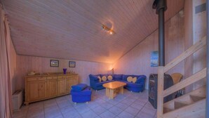 Um quarto aconchegante com teto de madeira, um conjunto de sofás, um armário de madeira e uma escada.