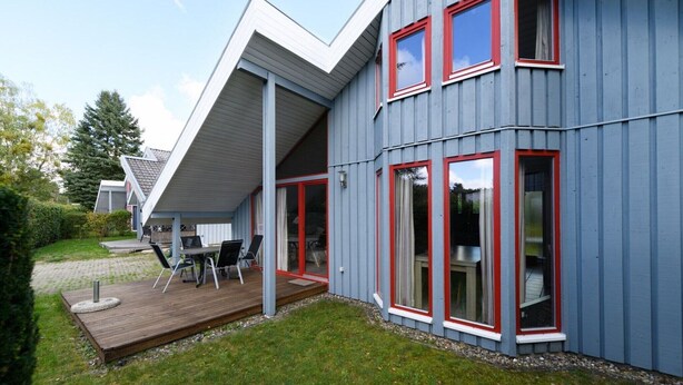 Uma casa moderna com um deck, janelas amplas e uma área externa coberta.