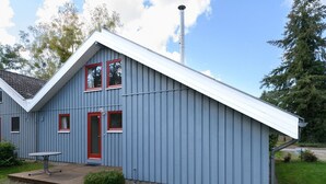 Um edifício azul com uma porta vermelha, uma chaminé e um pequeno alpendre com uma mesa.
