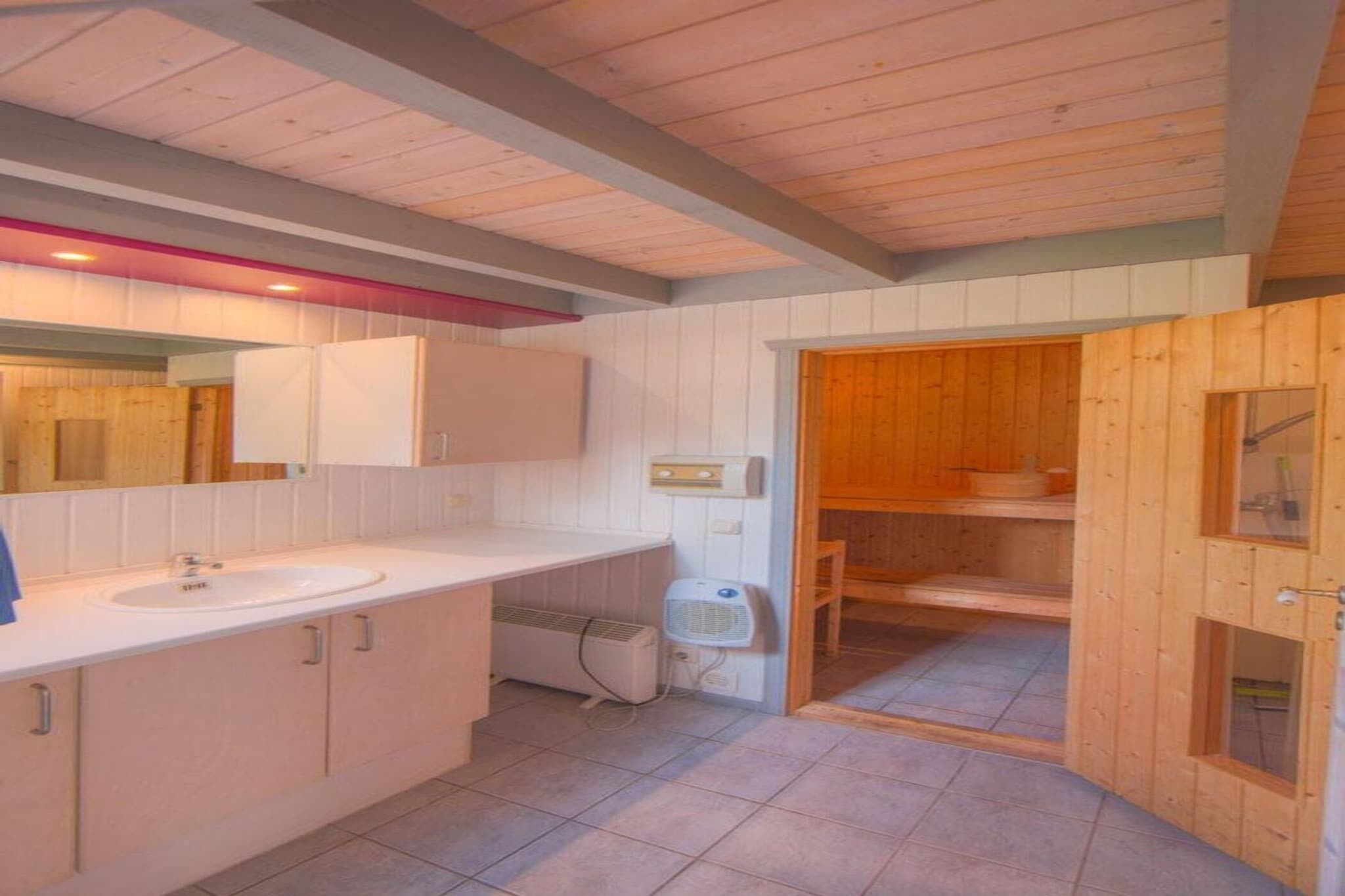 Une salle de bain comprenant un lavabo, un miroir, des placards et une porte en bois donnant accès à une zone douche.