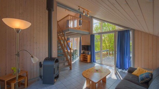 A cozy living room with a wooden staircase, a fireplace, and a large sliding glass door leading to an outdoor area. - skandinavisches Ferienhaus in Mirow (Granzow)