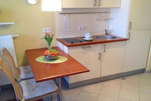 A small kitchen with a wooden table, a bowl of fruit, and a vase of flowers. - Elegant eingerichtete Ferienwohnung (Granzow)