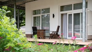 A covered outdoor seating area with a table and chairs, large windows, and a view of a garden with flowers. - Elegant eingerichtete Ferienwohnung (Granzow)