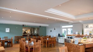 A spacious dining area with wooden tables and chairs, a buffet station, and a kitchen in the background. - Appartement mit skandinavischem Flair (Granzow)