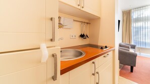 Eine moderne Küche mit Holzarbeitsplatte, Spüle aus Edelstahl und weißen Schränken. Ein Fenster mit Vorhängen bietet Blick auf Gebäude.