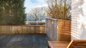 Eine Holzterrasse mit einer Holzbank, umgeben von einem Holenzaun und Bäumen.