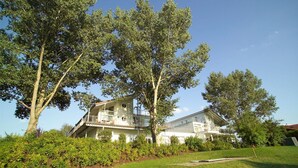 A two-story house with a balcony, surrounded by lush greenery and trees. - Gemütliches Appartement mit skandinavischem Flair (Granzow)