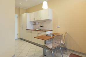 A compact kitchen with white cabinets, a wooden countertop, and a small dining table with two wicker chairs.