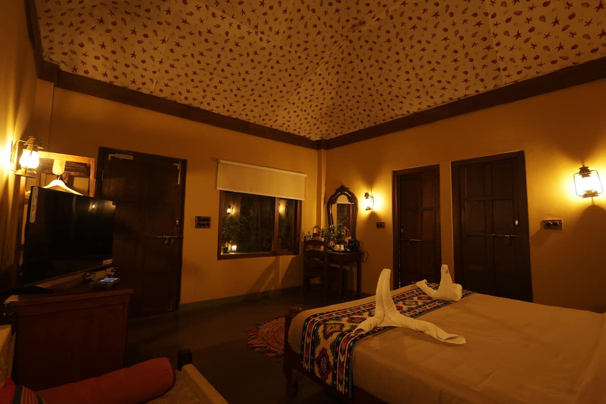 Habitación de hotel con cama, escritorio con televisor, ventana con vistas y luces en la pared.