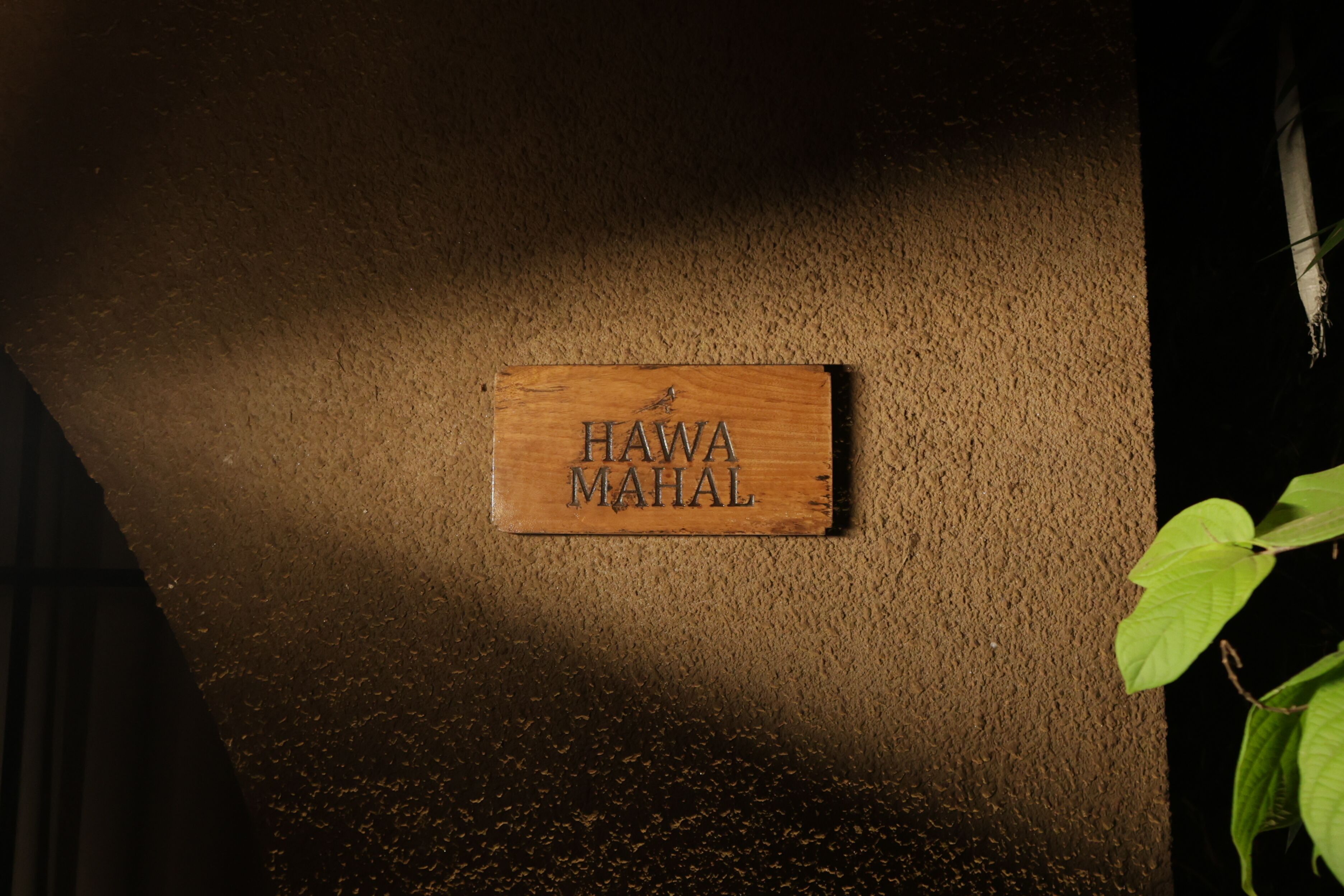 Una targa di legno con l'incisione "HAWA MAHAL" fissata a una parete strutturata.
