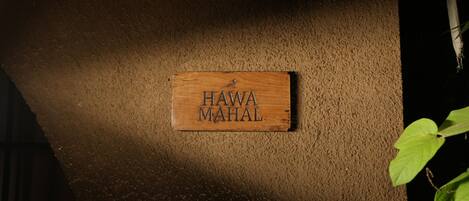 Una targa di legno con l'incisione "HAWA MAHAL" fissata a una parete strutturata.