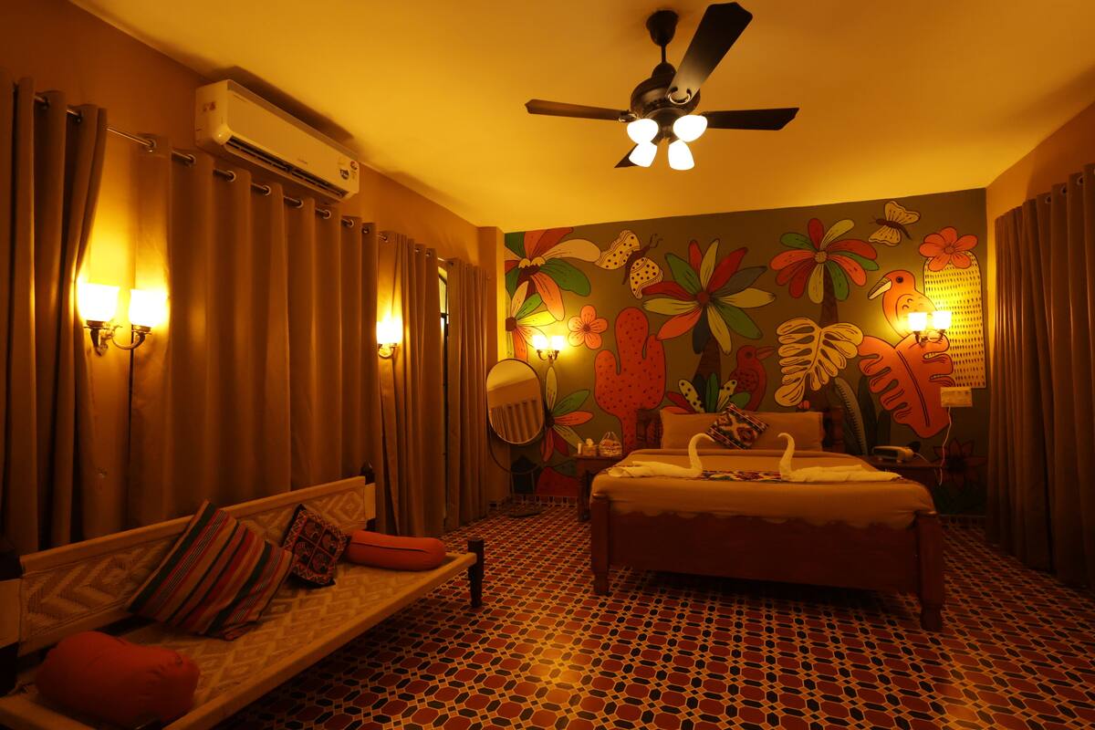 Una habitación de hotel con cama, sofá, ventilador de techo y pared decorada con un mural floral.