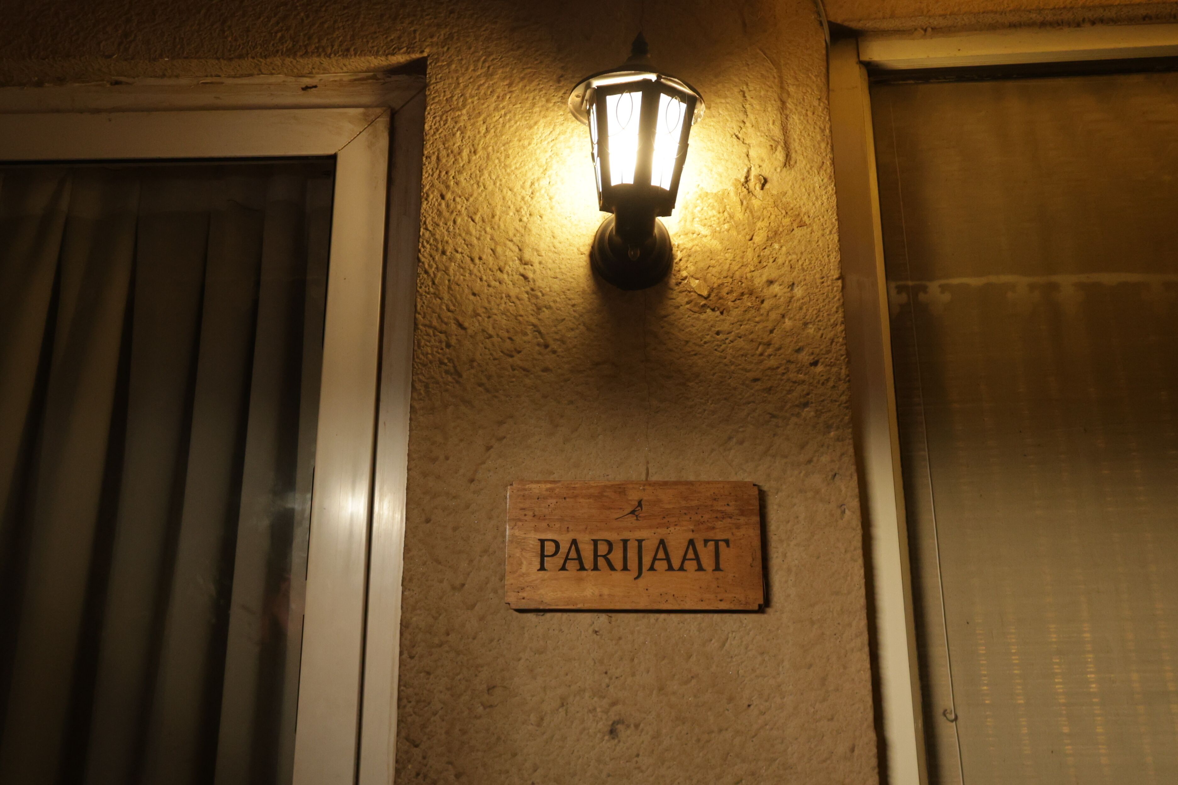 A wooden sign with the name "PARJAAT" mounted on a textured wall, next to a door with a metal handle and a light fixture above it.