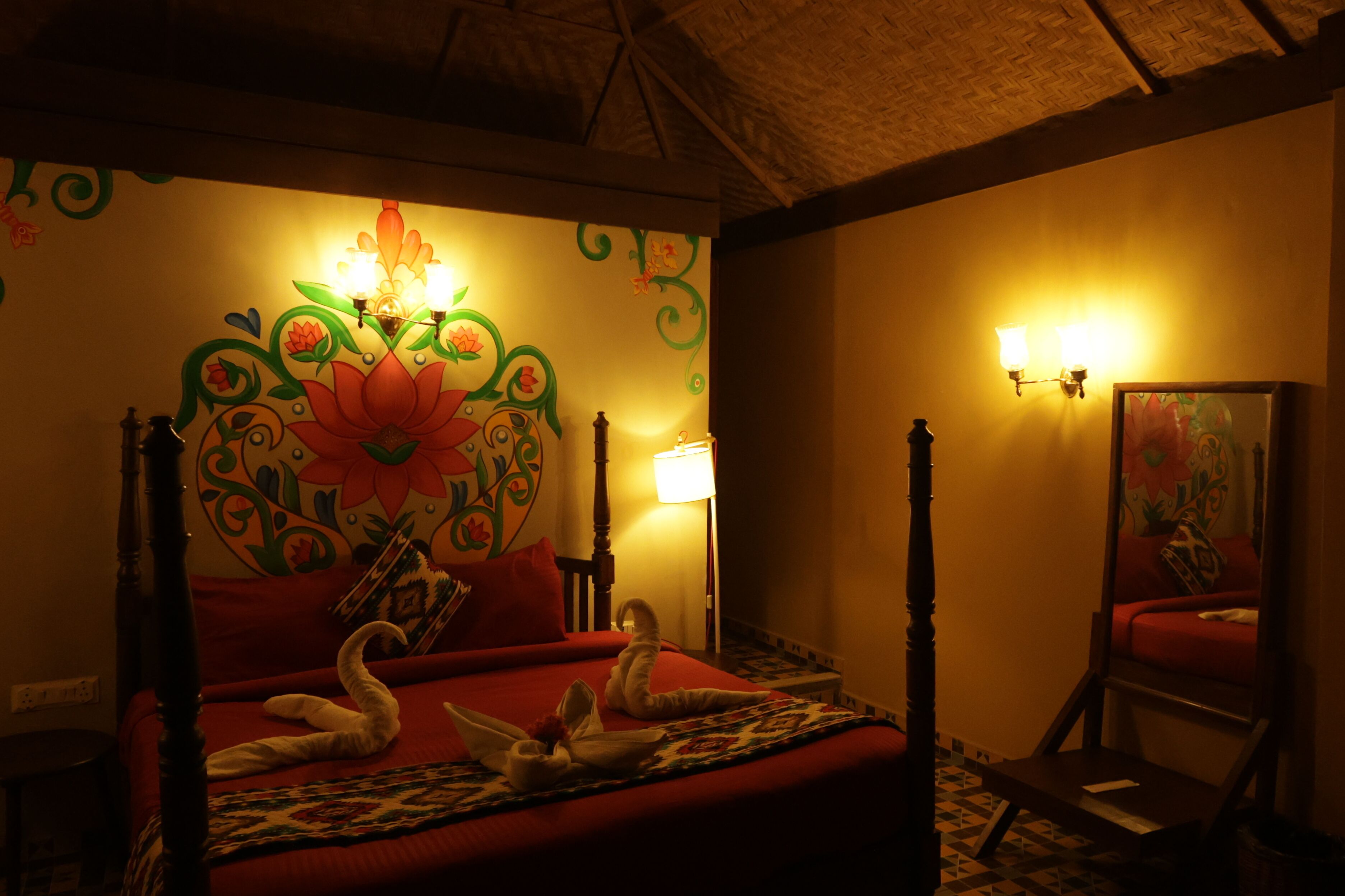 A room with a bed, a mirror, and a wall with floral artwork.