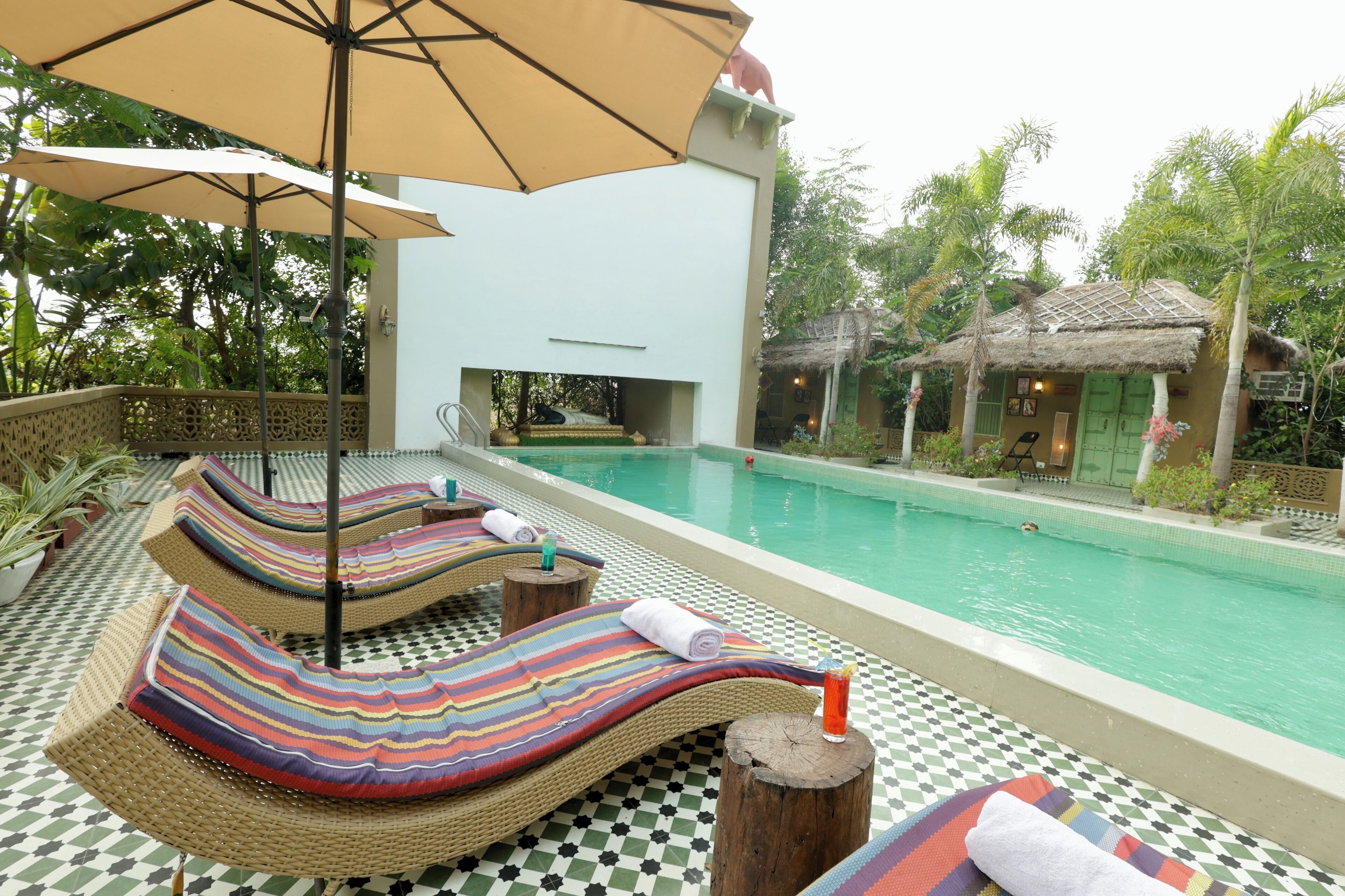 Zona de piscina con sillones, una piscina y una estructura con techo de paja.