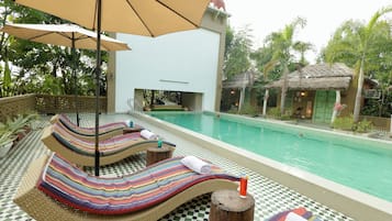 Zona de piscina con sillones, una piscina y una estructura con techo de paja.