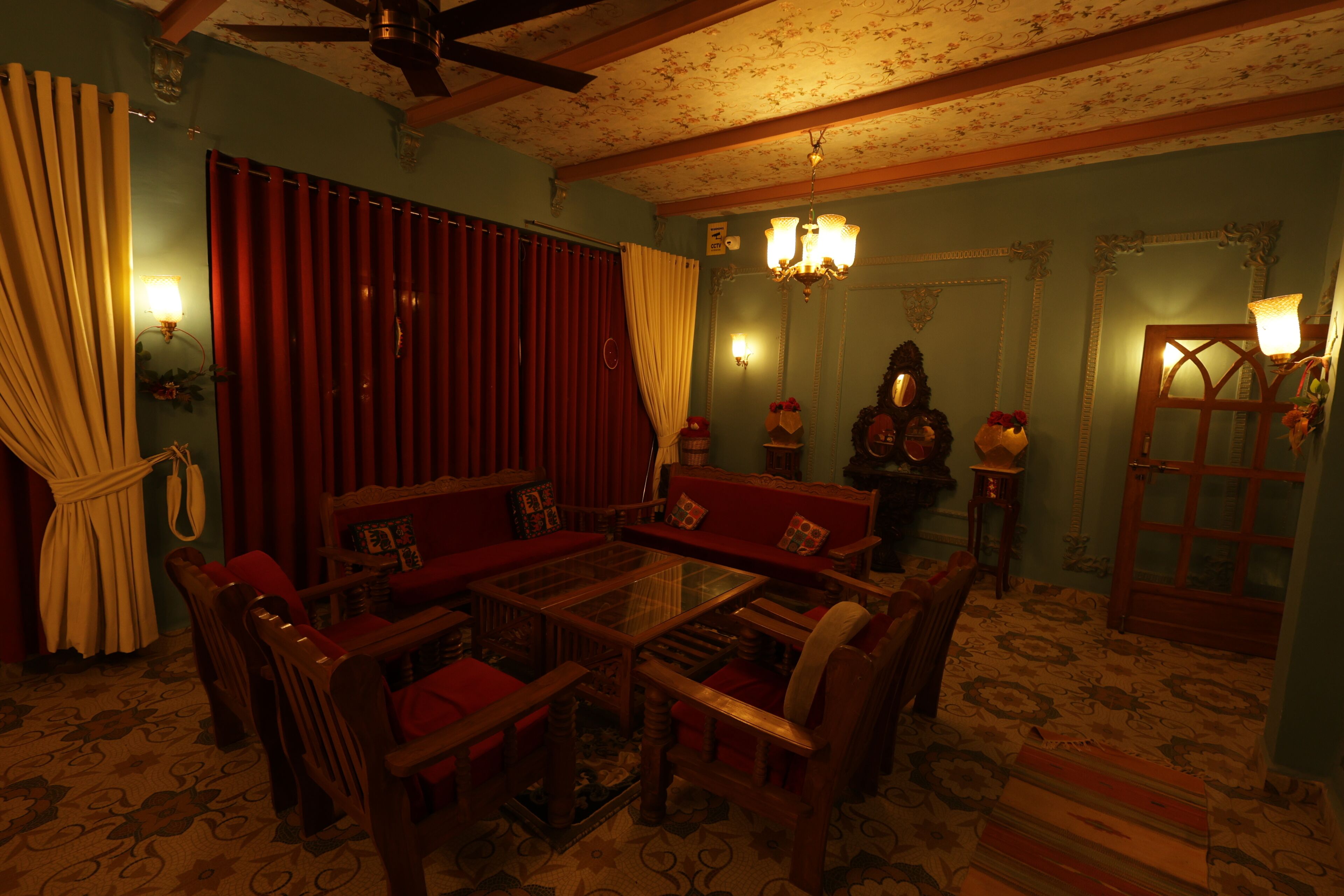 Quarto com mesa de centro de madeira, rodeado por cadeiras, um sofá e um tapete estampado.