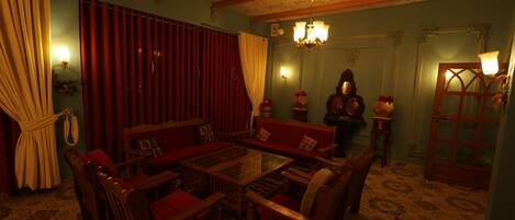 Quarto com mesa de centro de madeira, rodeado por cadeiras, um sofá e um tapete estampado.