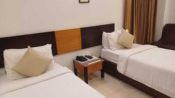 A hotel room with two single beds, a small bedside table with a phone and remote control, and a curtain on the window.