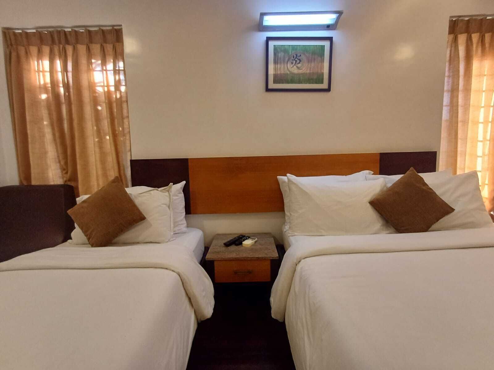 A hotel room with two beds, a nightstand, a remote control, and a framed picture on the wall.