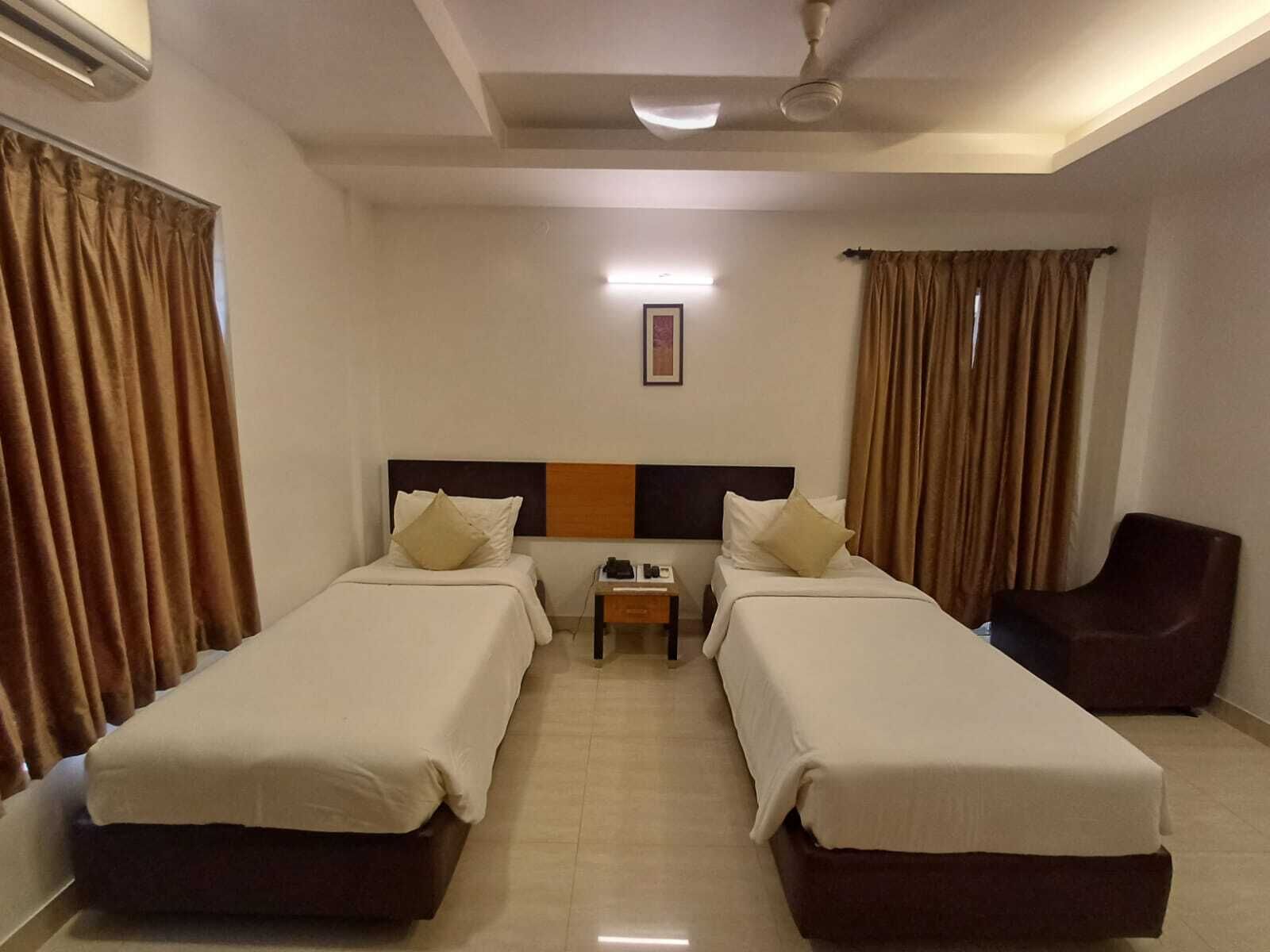 A hotel room with two single beds, a chair, a nightstand, and a ceiling fan.