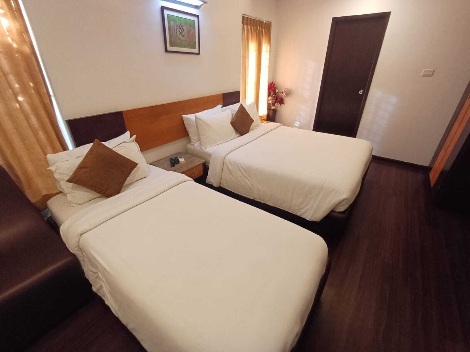 Une chambre d’hôtel avec deux lits simples, une tête de lit en bois, une table de chevet et un tableau encadré au mur.