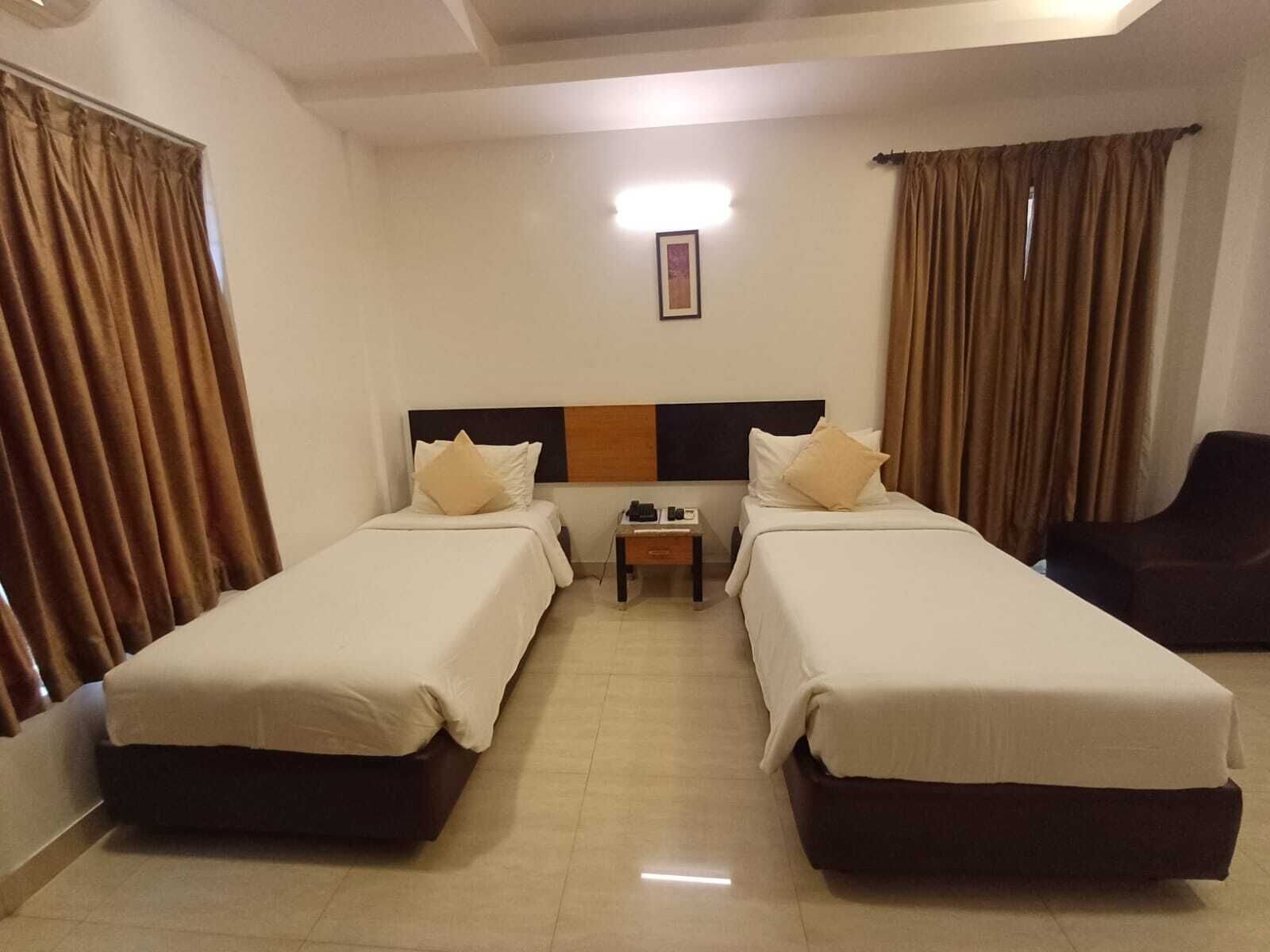 A hotel room with two single beds, a nightstand, a chair, and curtains.